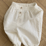 Auf einem Holzboden ist eine weiße Bebe Holic Natural Pants mit elastischem Bund und Knopfverschluss abgebildet. Die Hose hat eine lockere, bequeme Passform mit elastischen Beinöffnungen und ist damit ein vielseitiges Must-have für die Garderobe jedes Babys.