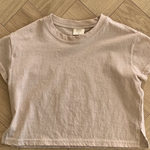 Ein Bebe Holic Basic Tee liegt flach auf einem Holzboden. Das Shirt aus hochwertiger Baumwolle hat einen runden Halsausschnitt und kleine Seitenschlitze am Saum. In der Nähe des Innenkragens ist ein Etikett zu sehen.