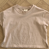 Ein Bebe Holic Basic Tee liegt flach auf einem Holzboden. Das Shirt aus hochwertiger Baumwolle hat einen runden Halsausschnitt und kleine Seitenschlitze am Saum. In der Nähe des Innenkragens ist ein Etikett zu sehen.