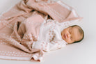 Ein Neugeborenes schläft friedlich auf einer hellen Unterlage, eingehüllt in eine rosa Decke mit weißen Mustern aus antiallergischer Baumwolle. Das Baby trägt ein weißes Outfit mit rosa Punkten, das zur Decke passt und eine weiche und heitere Atmosphäre schafft. Das verwendete Produkt ist das Newborn Pack Punkte rosa: 0 -3 Monat (56 cm) von micu micu.