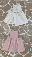 Auf einem gemusterten Steinboden sind drei Kinderkleider von Bebe Holic ausgestellt: zwei in Hellbeige und eines in Zartrosa, alle in schlichtem, elegantem Design, aus leichten Stoffen.