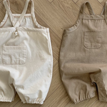 Zwei Twill-Bodysuits mit Taschen von Bebe Holic, einer weiß und einer beige, liegen flach auf einem Holzboden. Jeder hat eine Tasche auf der Vorderseite.