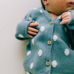 Ein Baby trägt eine übergroße blaue Jeansjacke mit Punkten: 3-6 Monate von micu micu. Das Gesicht des Babys ist teilweise sichtbar und seine Hand hält den Saum der Jeansjacke. Der Hintergrund ist in einer sanften, hellen Farbe gehalten.