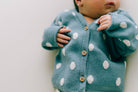 Ein Baby trägt eine übergroße blaue Jeansjacke mit Punkten: 3-6 Monate von micu micu. Das Gesicht des Babys ist teilweise sichtbar und seine Hand hält den Saum der Jeansjacke. Der Hintergrund ist in einer sanften, hellen Farbe gehalten.