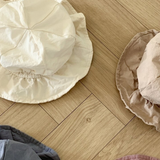 Vier zerknitterte Crunch Bucket Hats von Bebe Holic in einer natürlichen Farbpalette aus Weiß, Beige, Blau und Kastanienbraun sind auf einem hölzernen Boden mit Fischgrätenmuster ausgebreitet. Die Hüte scheinen aus einem leichten, lässigen Stoff gefertigt zu sein.