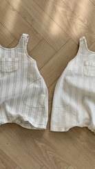 Zwei Bebeholic Ariel St Body Suit Kleinkinder-Overalls liegen flach auf einem Holzboden, einer mit vertikalen Streifen und einer Vordertasche, der andere mit horizontalen Streifen und zwei Taschen.