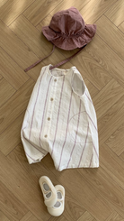 Ein hellgestreiftes Bebe Holic Daisy ST Body Suit-Outfit, bestehend aus einem ärmellosen Oberteil und einer dazu passenden Mütze, kombiniert mit weißen Schuhen, ordentlich auf einem Holzboden angeordnet.