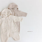 Zwei Baby-Strampler mit Kapuze, oder Hoody Bodysuits, liegen flach auf einem weißen Hintergrund. Der linke Strampler ist cremefarben und hat Vordertaschen, der rechte ist taupe. Unter den Hoody Bodysuits ist in Kleinbuchstaben der Text „Bebe Holic“ aufgedruckt.